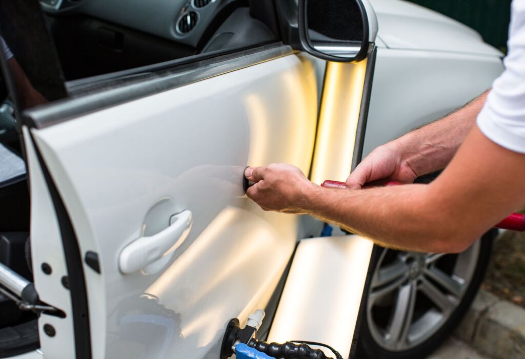Technician repairing a dent on a white car door.
