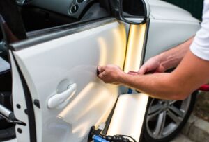 Technician repairing a dent on a white car door.