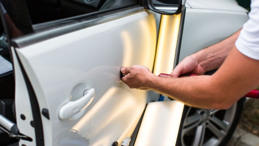 Technician repairing a dent on a white car door.