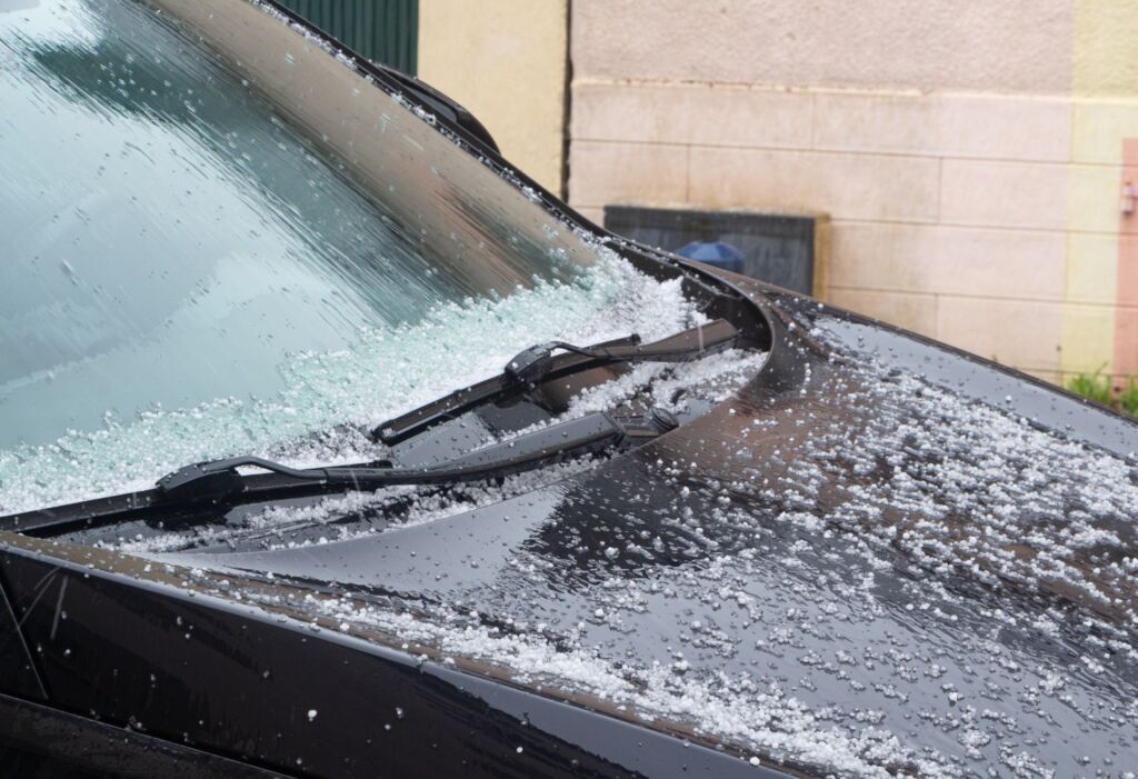 Hailstones covering a black car hood and windshield.