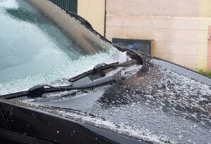 Hailstones covering a black car hood and windshield.