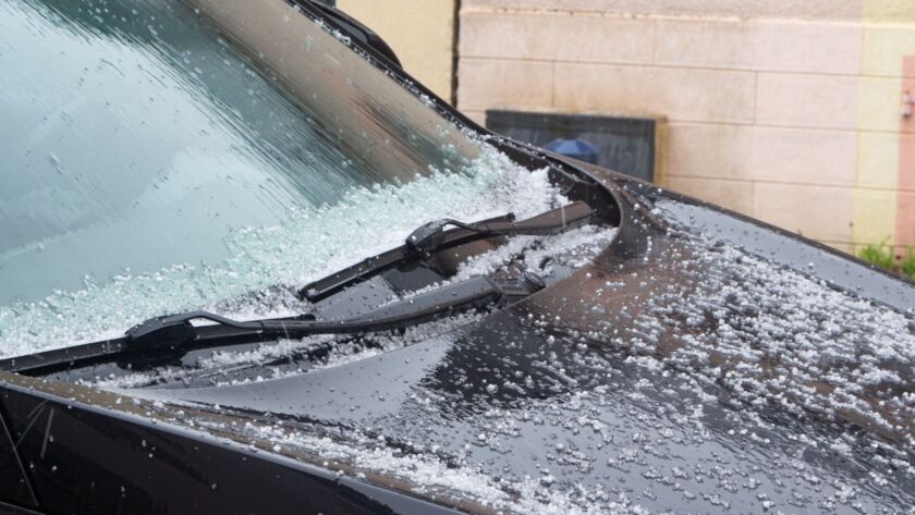 Hailstones covering a black car hood and windshield.