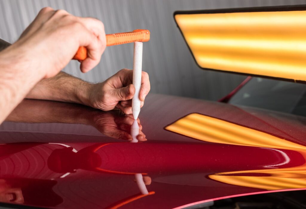 Technician tapping a dent on a red car panel.