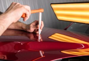 Technician tapping a dent on a red car panel.