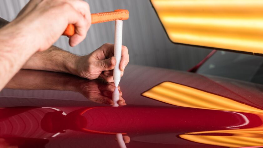 Technician tapping a dent on a red car panel.