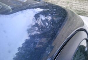 Close-up of hail dent damage on a black car roof.