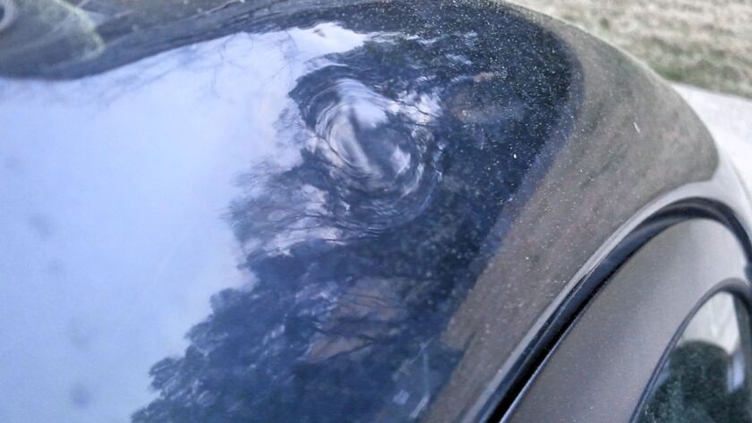 Close-up of hail dent damage on a black car roof.