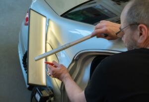 Technician repairing a car dent using paintless dent tools.