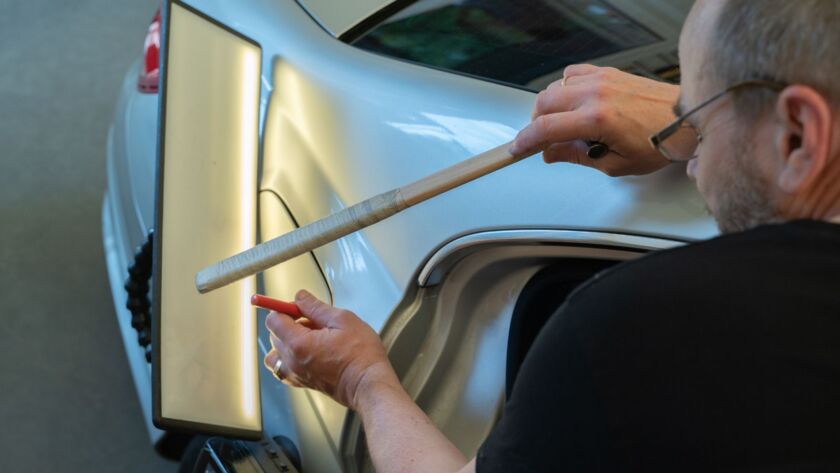 Technician repairing a car dent using paintless dent tools.