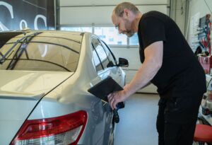 Technician inspecting a silver car door for dents.