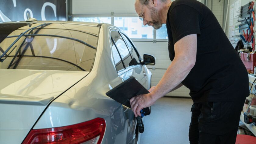 Technician inspecting a silver car door for dents.