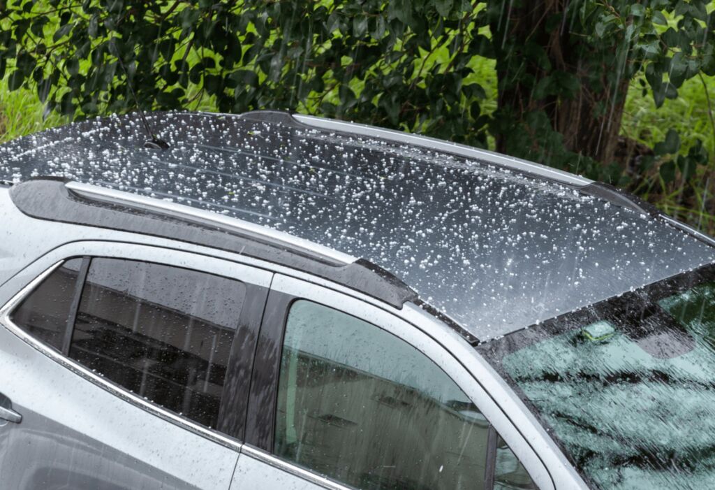 Hailstones falling on the roof of a white SUV.