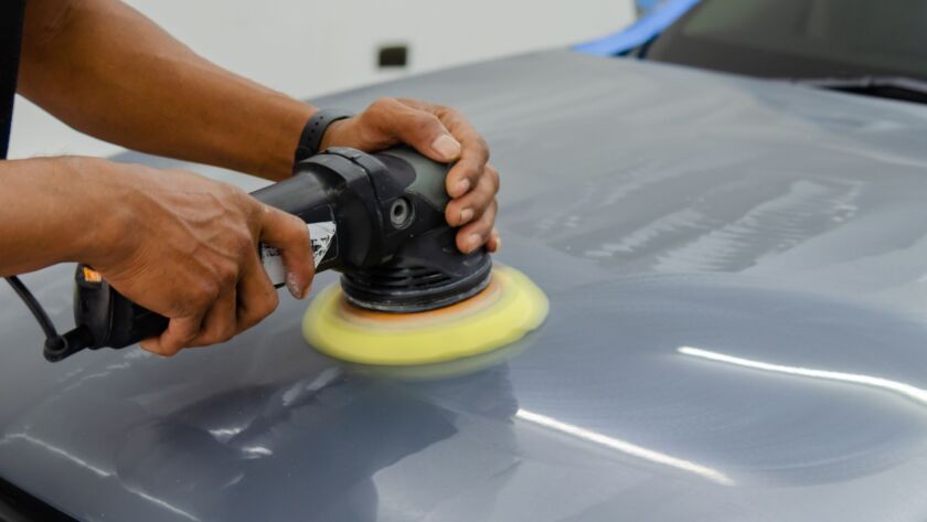 Technician polishing a gray car hood with a buffer.