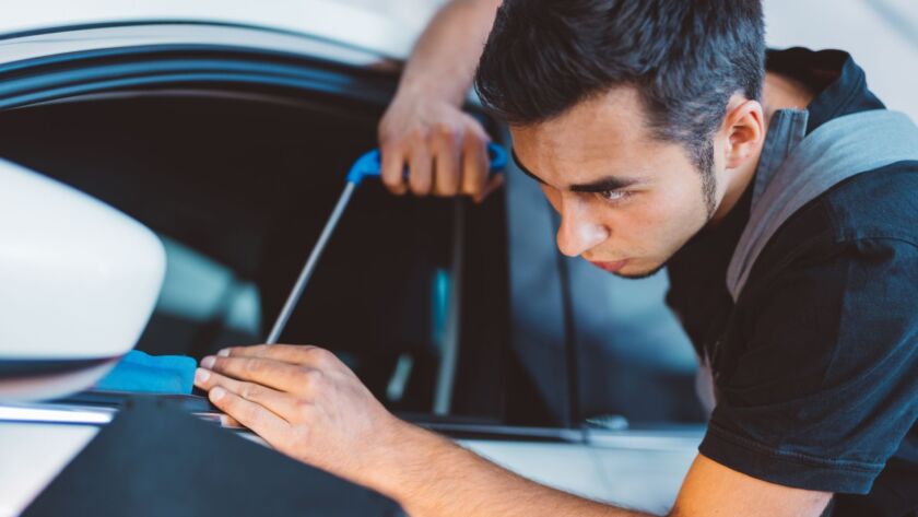 Technician cleaning a car window with a detailing tool.