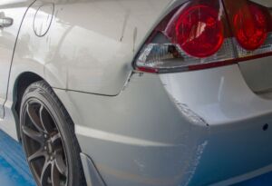 Scratched rear bumper and taillight area on a white car.