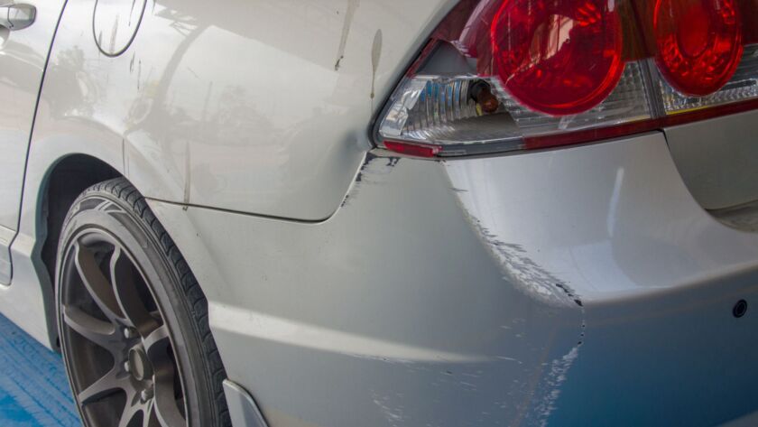 Scratched rear bumper and taillight area on a white car.