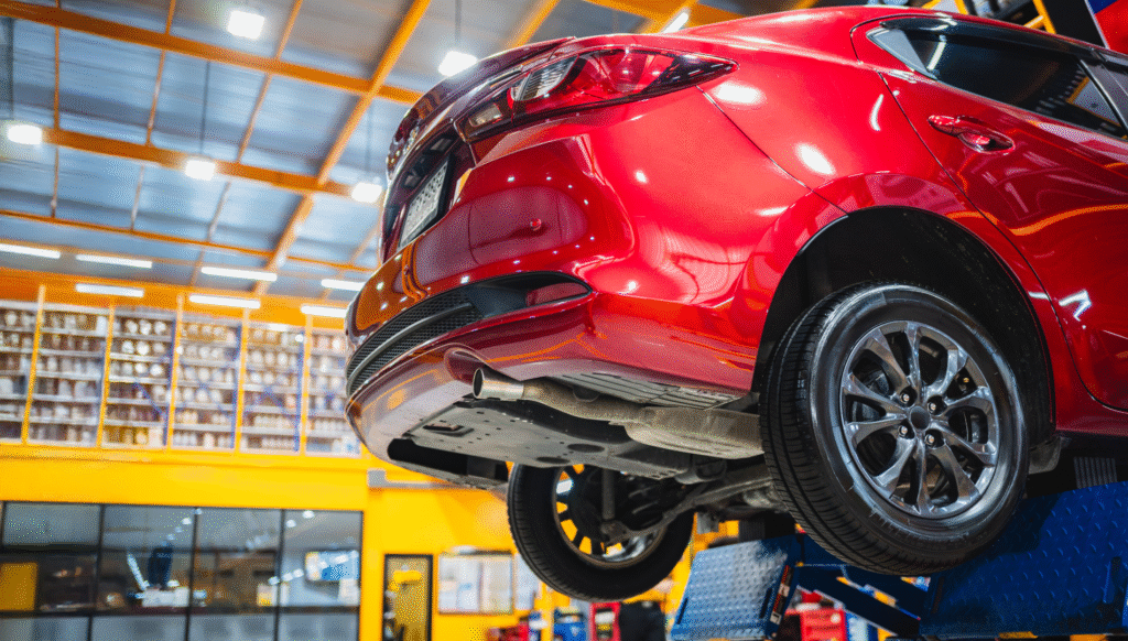 Red car raised on a lift in an auto repair shop.