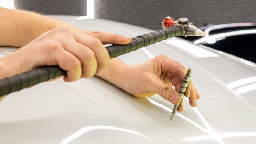Paintless dent repair tool fixing hail damage on car roof