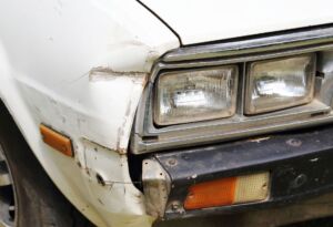 Old car front end with rust, scratches, and bumper damage