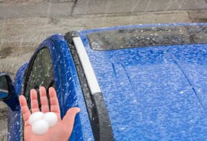 Large hailstones on hand beside hail-damaged blue car
