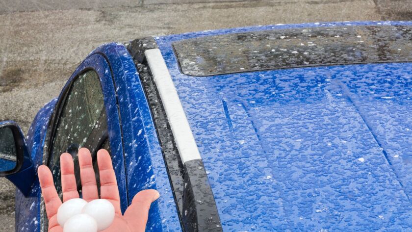 Large hailstones on hand beside hail-damaged blue car