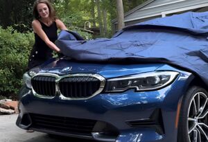 Woman covering a blue car to protect it from hail damage